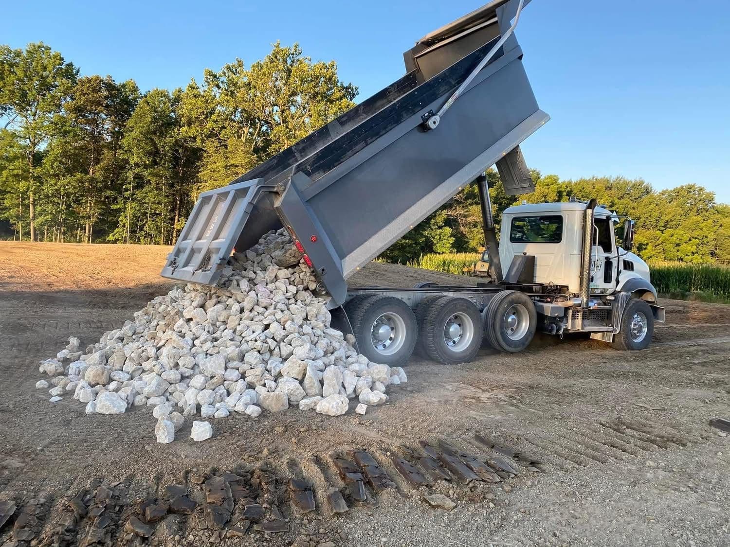 A tri-axle dump truck tipping a load of clean stone on a graded site.