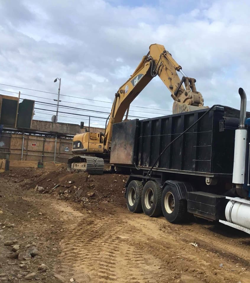 An excavator loading excavated soil into a tri-axle dump truck.